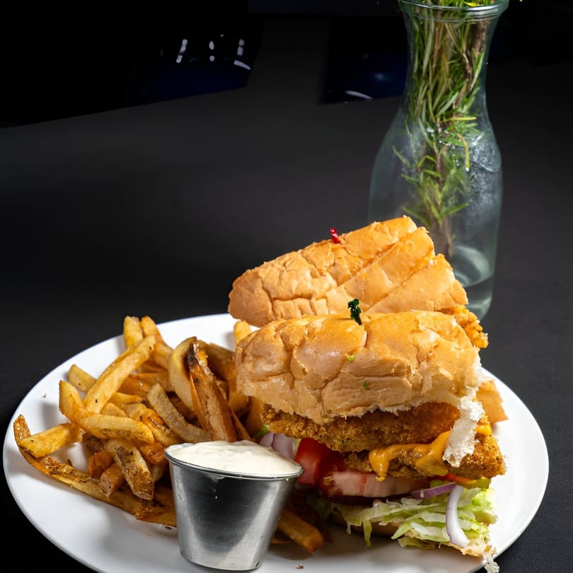 McClellan's Fish and Chicken's fried fish sandwich with fries and dipping sauce on a white plate.