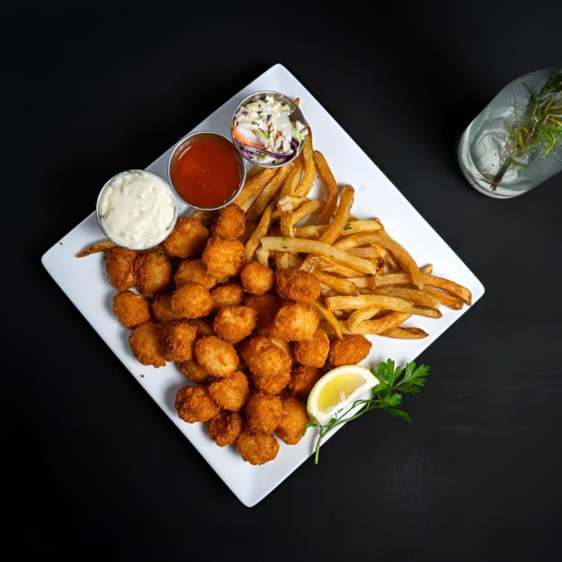 A white plate of McClellan's fried scallops and french fries with coleslaw, cocktail sauce, and tartar sauce.