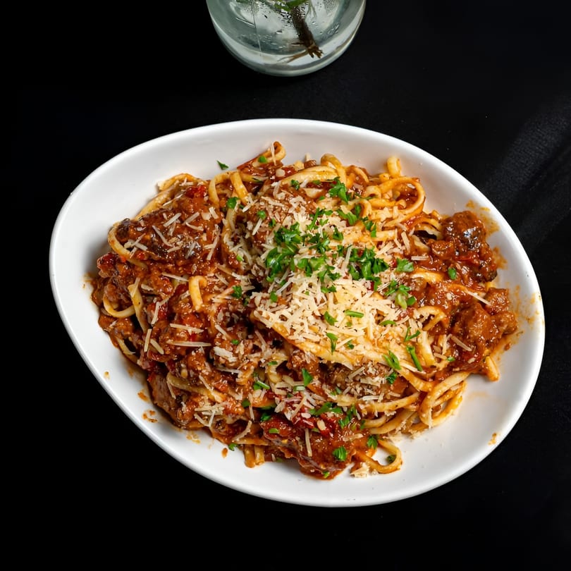 A white oval bowl filled with spaghetti and meatballs, topped with parmesan cheese and parsley.