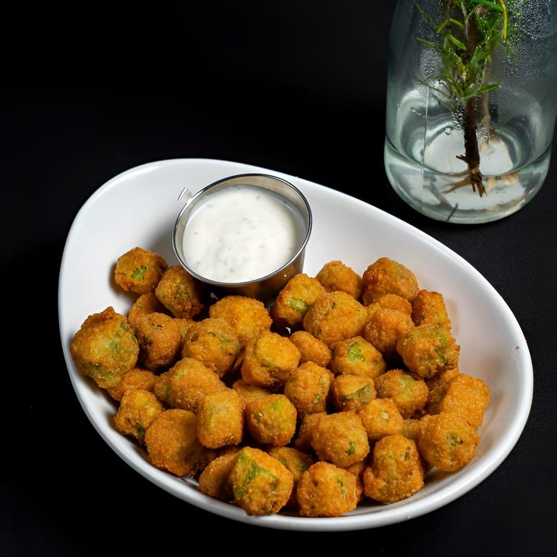 A white bowl filled with golden-brown fried okra and a side of creamy dipping sauce.