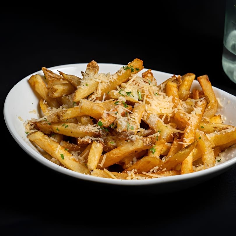 A white bowl filled with golden-brown french fries, topped with grated Parmesan cheese and parsley.