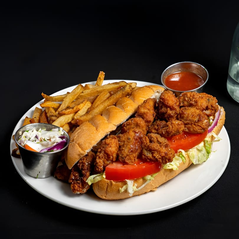 McClellan's Fish and Chicken's fried oyster po'boy with fries, coleslaw, and ketchup on a white plate.